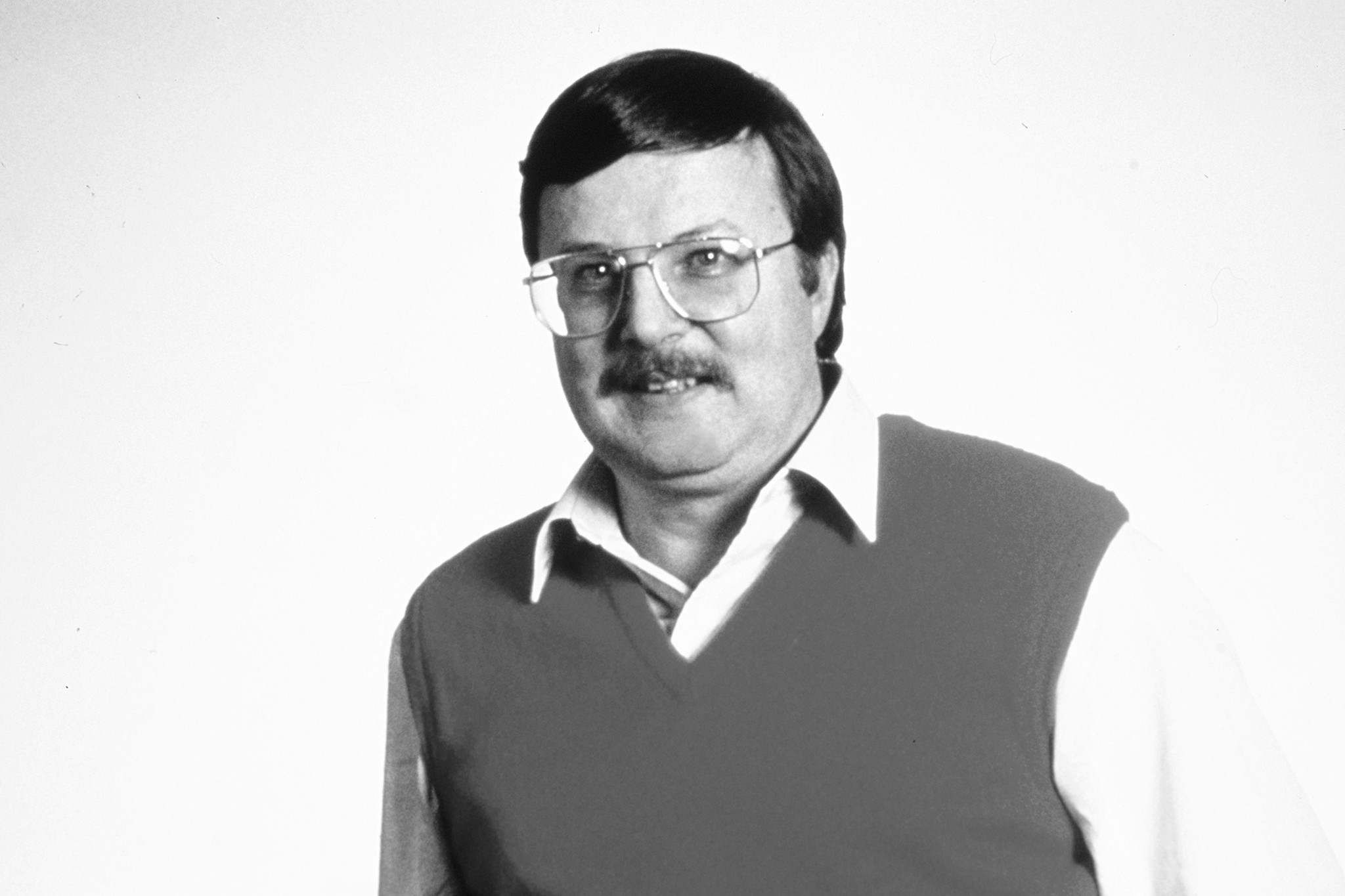 Schwarzweiss-Foto von Peter Hotz mit Brille und Schnurrbart, der ein Hemd und einen Pullover trägt.
