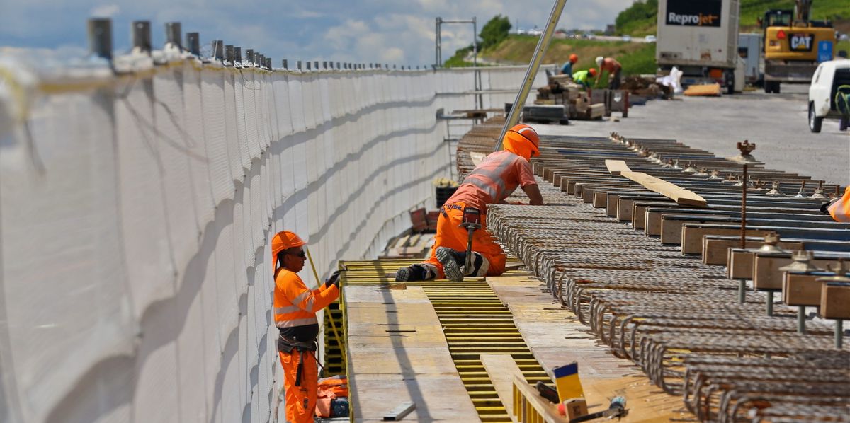 Deux ouvriers en construction portant des vêtements de sécurité orange travaillent sur une section d'un pont de l'autoroute A9, près de Chardonne.