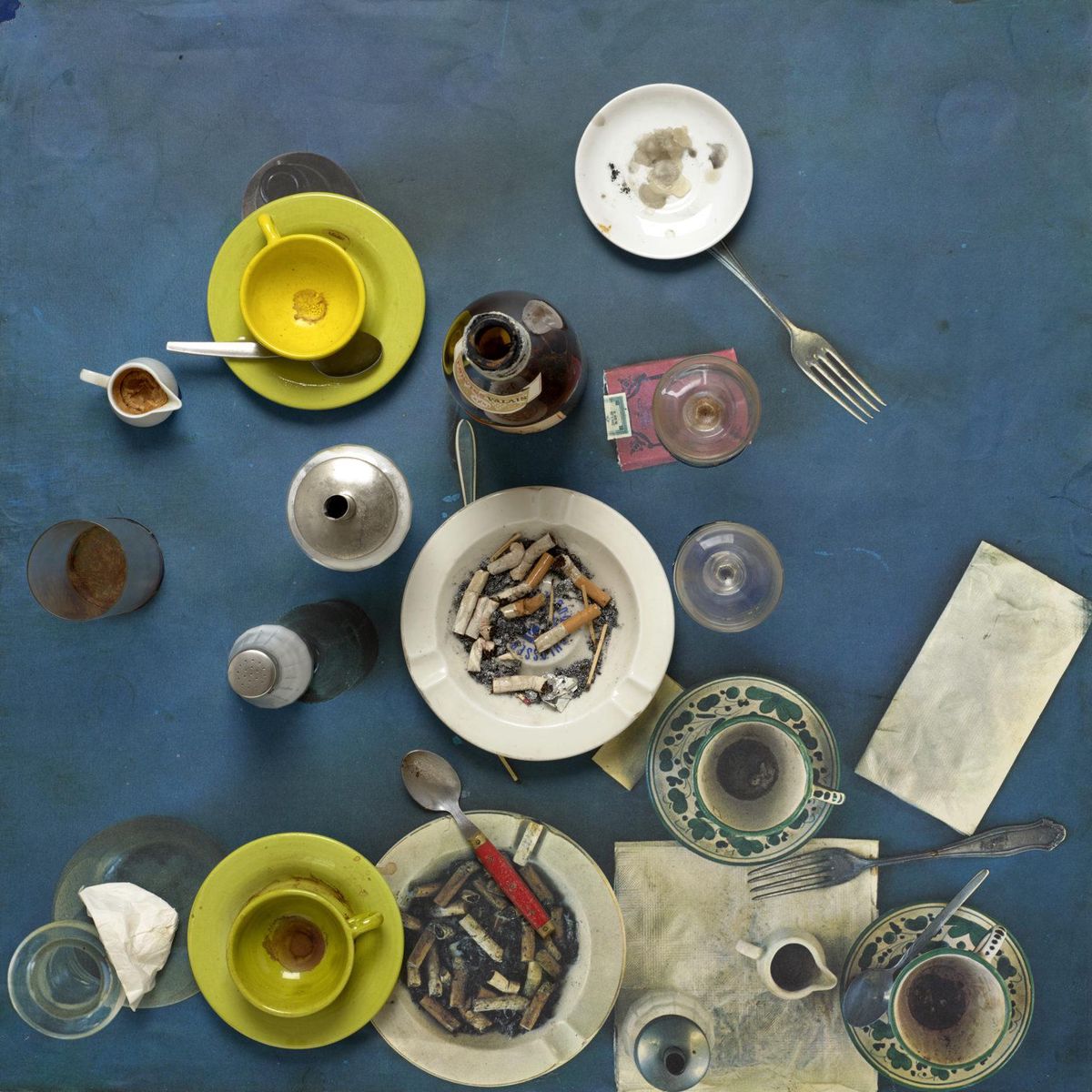 Assemblage artistique de Daniel Spoerri avec divers objets, y compris assiettes, couverts et tasses, disposés sur une photocopie collée.