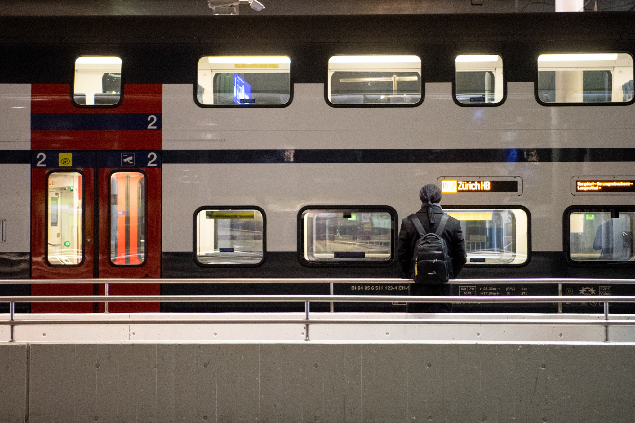 Ein Mann mit Rucksack steht auf einem Bahnsteig im Bahnhof Bern vor einem Zug, der nach Zürich fährt.