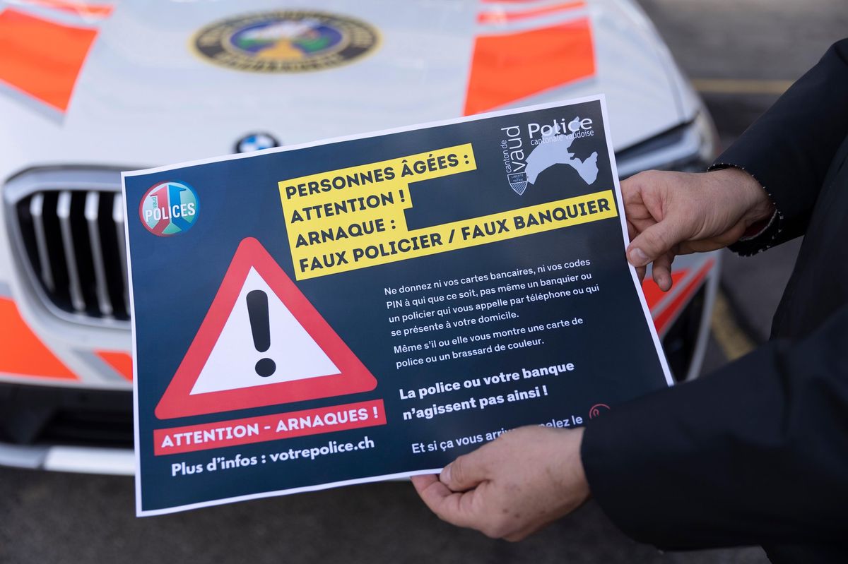 Un responsable tient une affiche d’avertissement contre les arnaques aux faux policiers à Lausanne, devant une voiture de police.