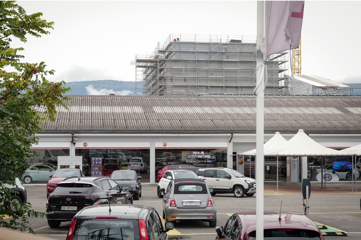Un garage Stellantis &You Genève à Meyrin avec plusieurs voitures garées devant et un bâtiment en construction à l'arrière-plan.