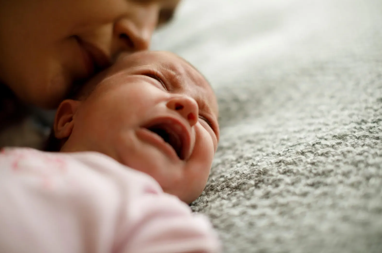 Un nourrisson pleure à côté de sa maman.