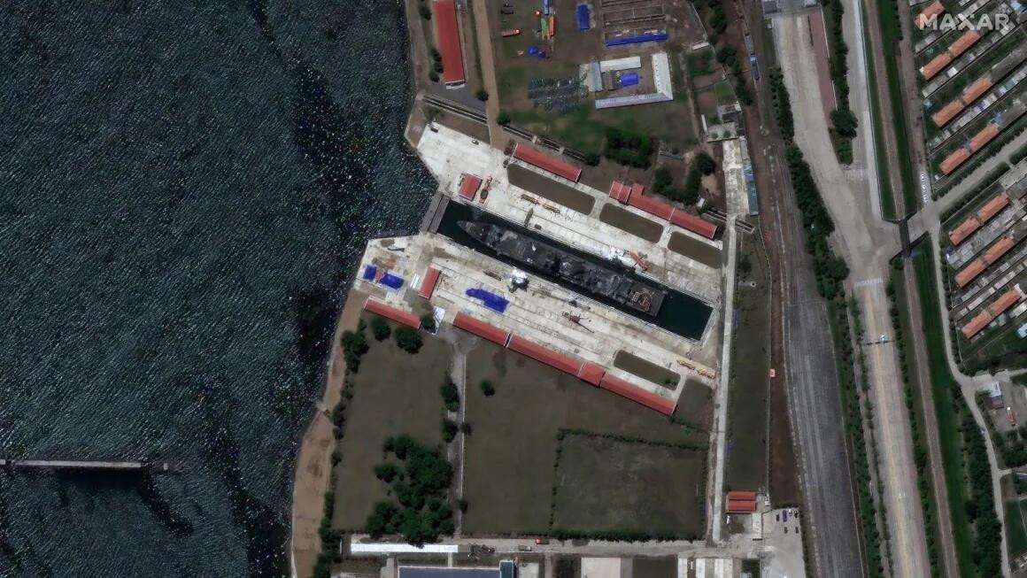 Satellitenbild eines grossen Trockendocks mit einem Schiff im Bau, umgeben von Gebäuden und einer angrenzenden Küstenlinie.