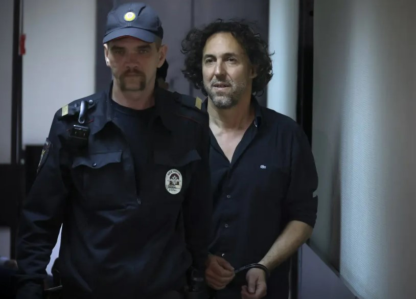 Un homme menotté escorté par un policier en uniforme dans un couloir.