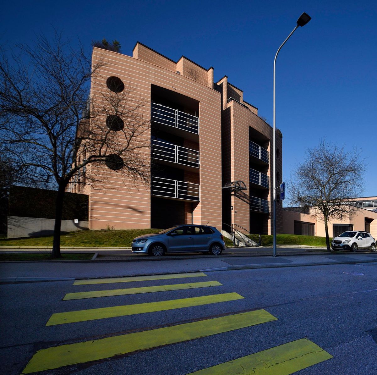 Vue des bâtiments du tribunal d’arrondissement de la Côte à Nyon, avec un ciel bleu clair et des voitures stationnées devant.