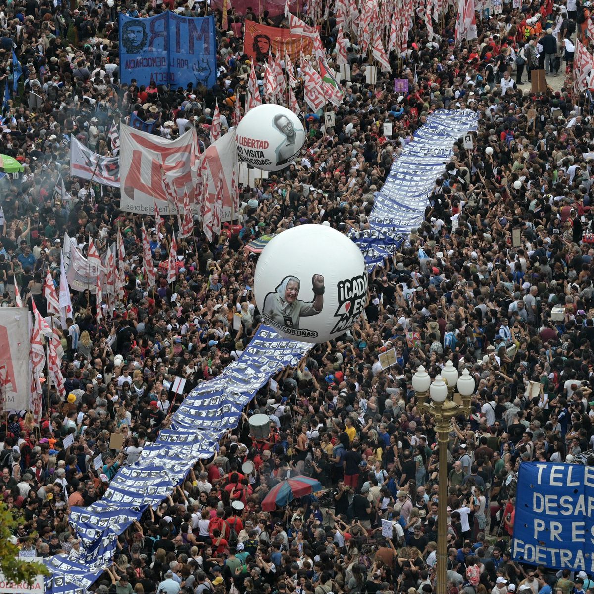 Une foule dense se rassemble sur la Plaza de Mayo à Buenos Aires pour commémorer le 49e anniversaire du coup d’État militaire de 1976. Un ballon avec le portrait de Nora Cortinas, activiste des Mères de la Plaza de Mayo Ligne Fondatrice, est visible parmi la foule. Des banderoles et des drapeaux entourent la place tandis que le gouvernement du président argentin Javier Milei annonce la déclassification des documents de la dernière dictature militaire.