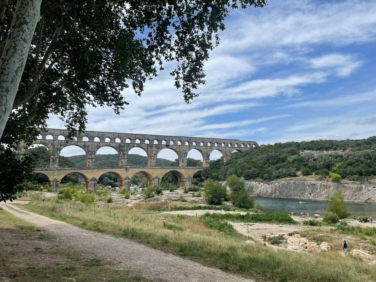 Pont aqueduc romain surplombant la rivière dans un paysage champêtre sous un ciel partiellement nuageux.