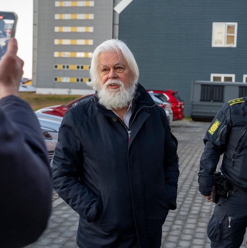 Activiste anti-chasse à la baleine devant un bâtiment avec un policier à Nuuk, Groenland, décembre 2024.