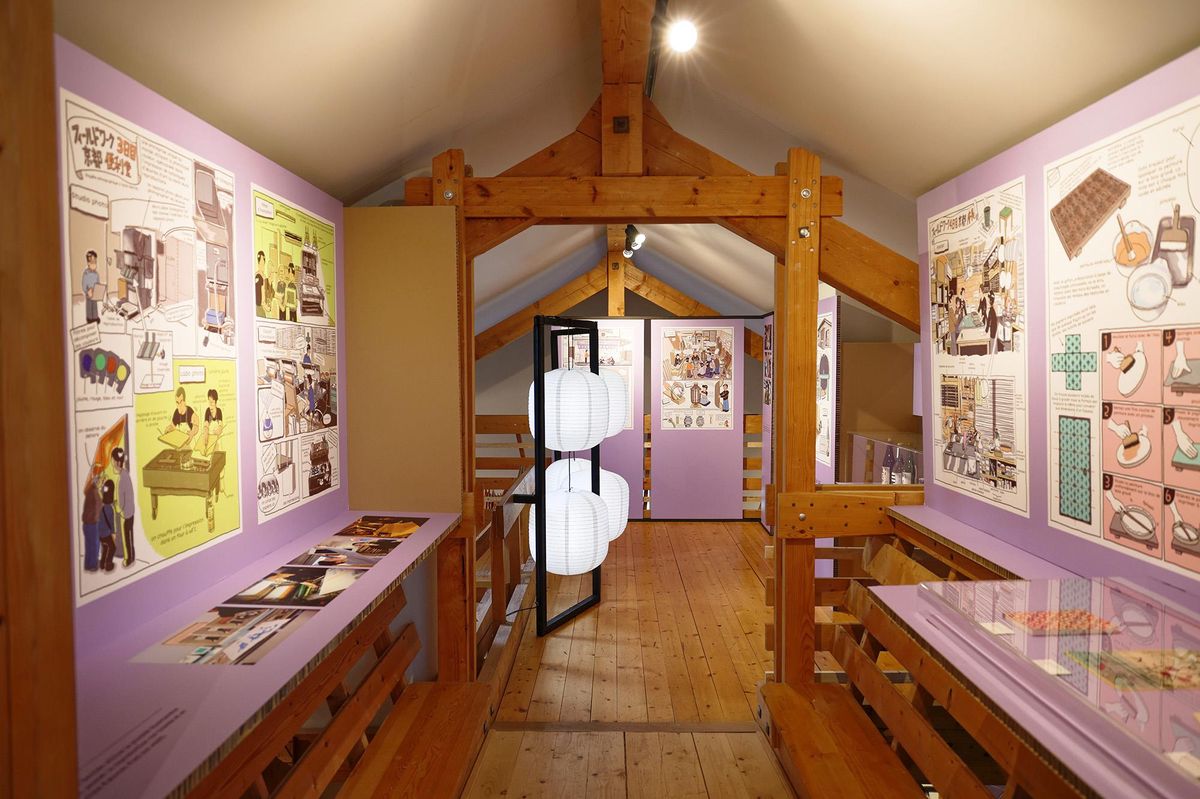 Exposition avec des illustrations et bandes dessinées sur des panneaux muraux violets, dans une salle en bois.