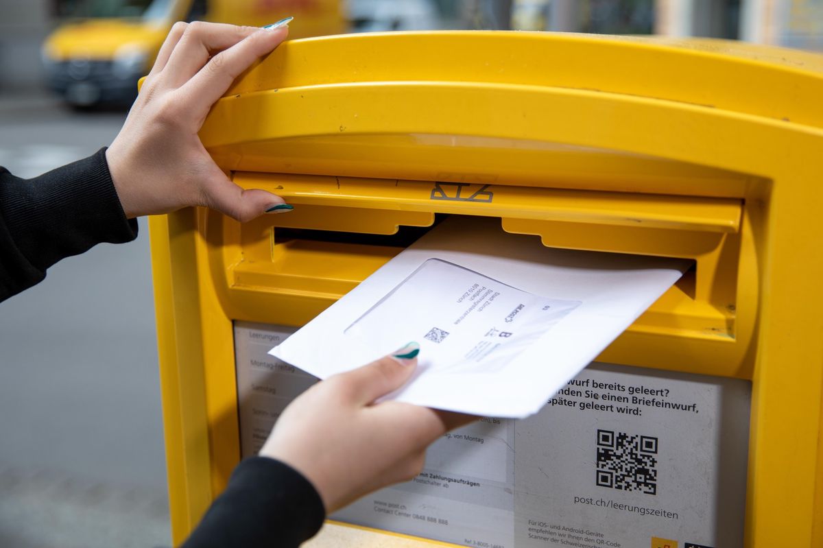 Personne insérant une enveloppe de vote dans une boîte aux lettres jaune.
