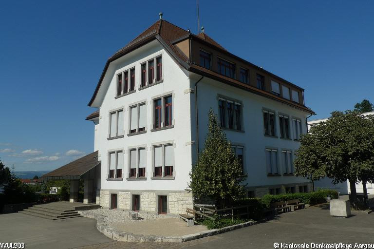 Altes Schulhaus Dorf: Weisses, mehrstöckiges Gebäude mit rotem Satteldach und Dachgauben unter blauem Himmel. Altes Schulhaus Dorf: Weisses, mehrstöckiges Gebäude mit rotem Satteldach und Dachgauben unter blauem Himmel.