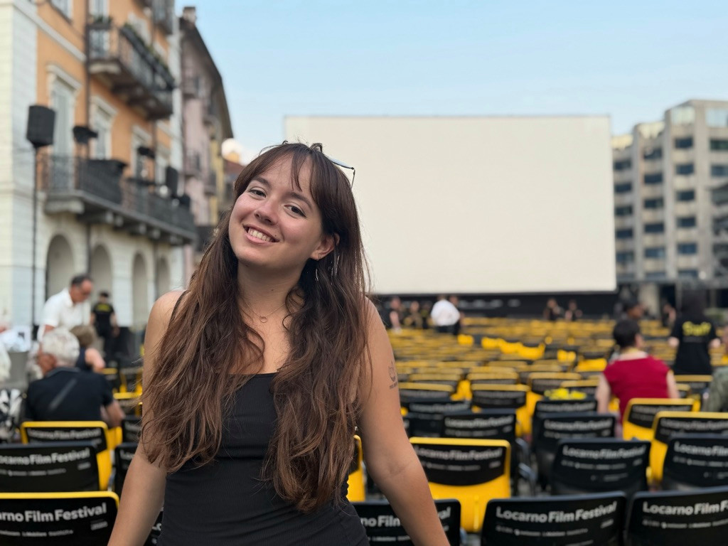 Jeune femme souriant devant un écran géant lors d’un festival de film en plein air avec des chaises pliantes alignées.