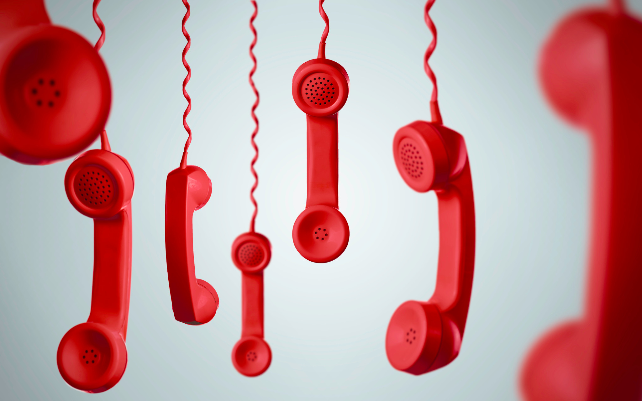 Mehrere rote Telefonhörer hängen an spiralförmigen Kabeln vor einem hellgrauen Hintergrund.