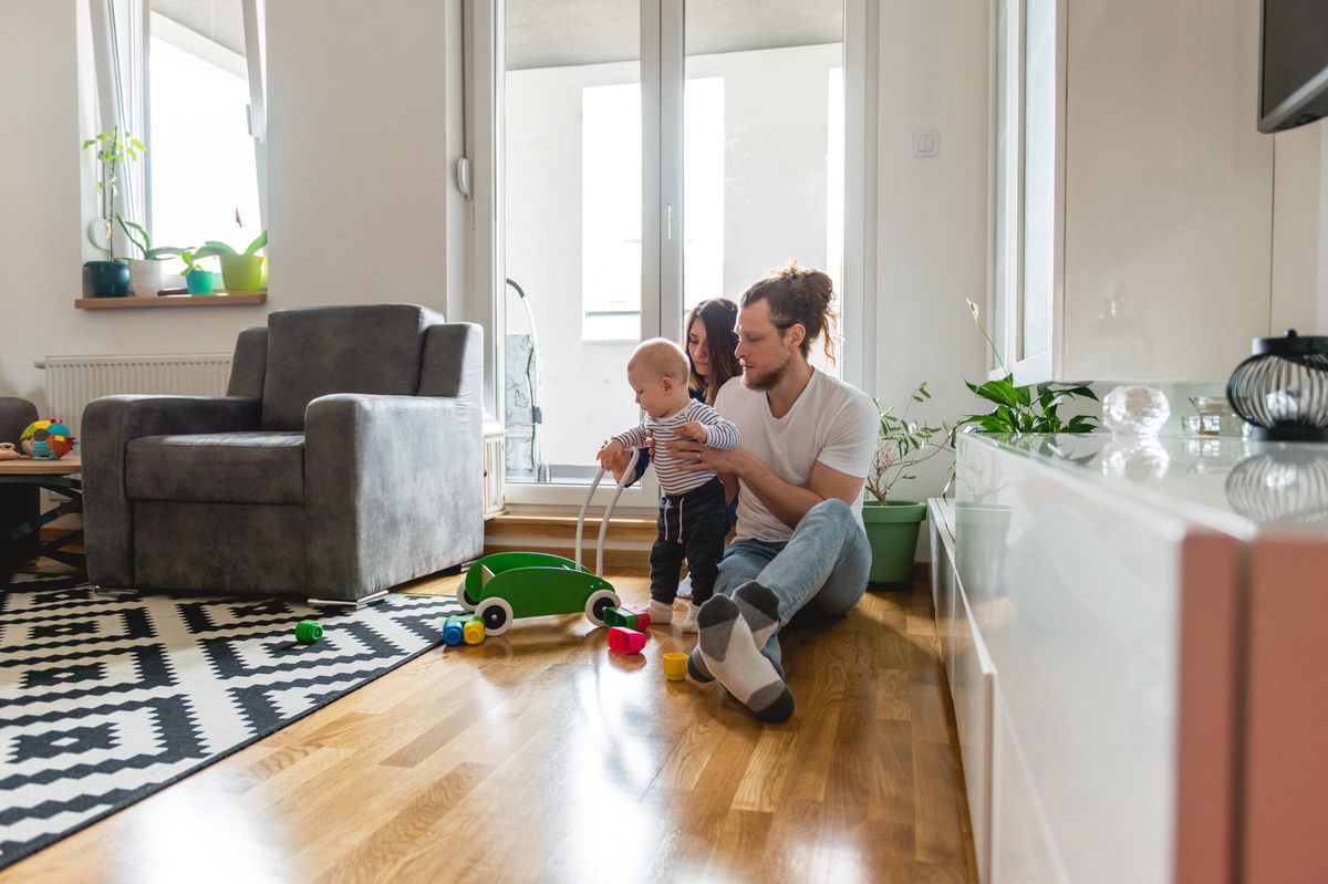 Jeune famille assise par terre avec un petit garçon, jouant dans un salon lumineux.