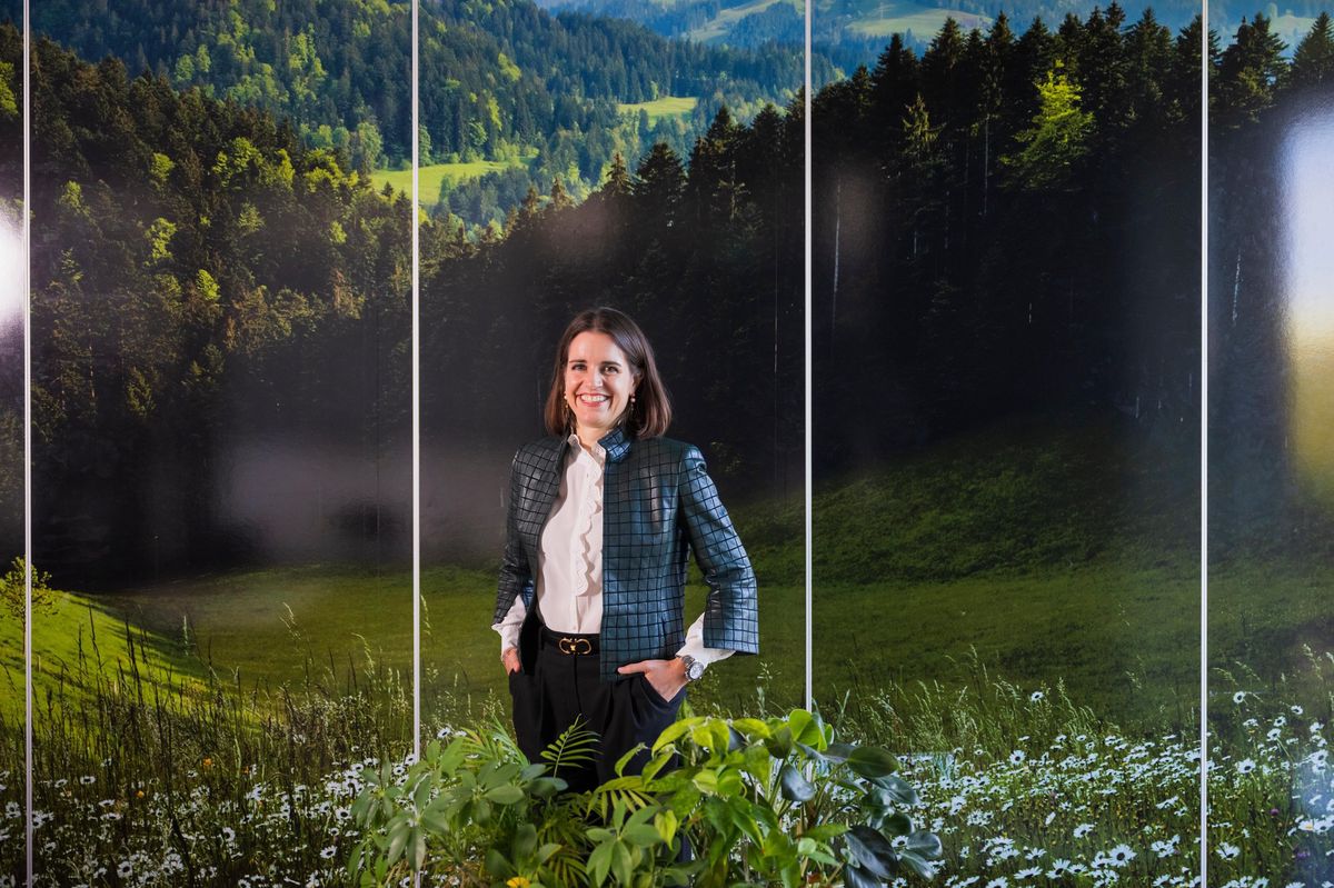 Ricarda Demarmels, CEO d'Emmi Schweiz, posant devant un paysage forestier verdoyant, avec des plantes à l'avant-plan.