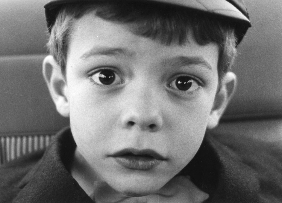 Gros plan en noir et blanc d'un jeune garçon avec un chapeau, regardant directement l'appareil photo avec une expression sérieuse.