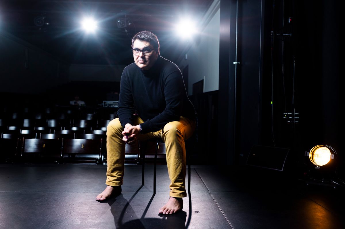 Fred Mudry, comédien et humoriste, en répétition à Boulimie, assis sur une chaise sur une scène sombre avec des projecteurs allumés en arrière-plan, à Lausanne le 19 septembre 2024.