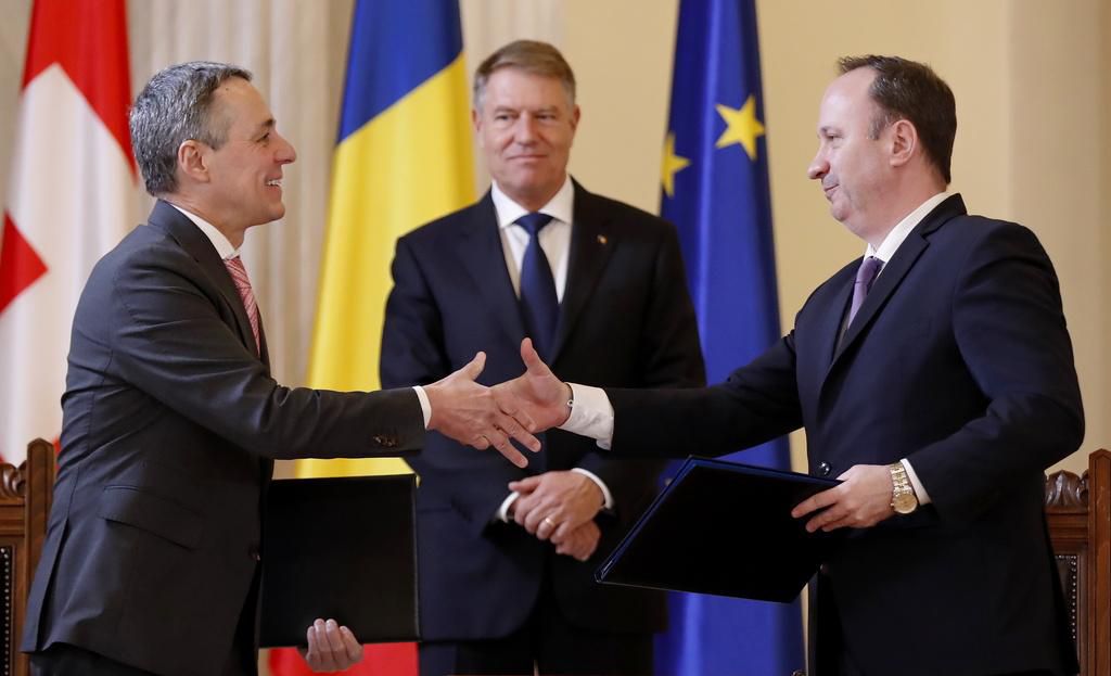 Le président de la Confédération suisse Ignazio Cassis et le ministre roumain des Finances, Adrian Caciu, sous les yeux du président roumain Klau Iohannis se serrent la main après avoir signé un traité d’assistance.