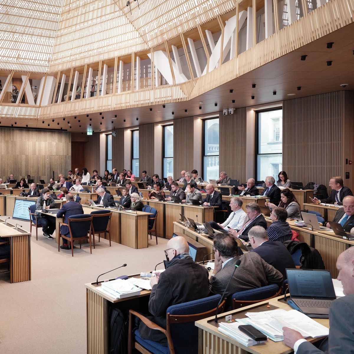 Session du Grand Conseil à Genève le 12 décembre 2024, discutant du Budget 2025, avec plusieurs participants assis dans une salle de réunion.
