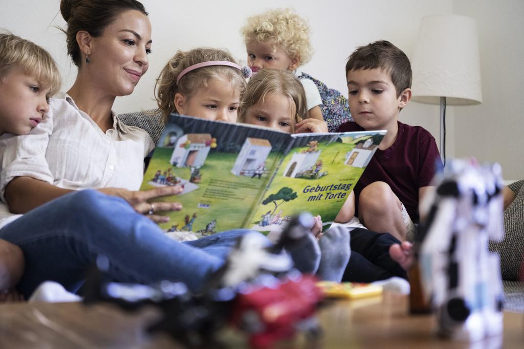 Eine Tagesmutter schaut nach dem Mittagessen auf dem Sofa mit den von ihr betreuten Kinder ein Kinderbuch an. (7. Juli 2020) 