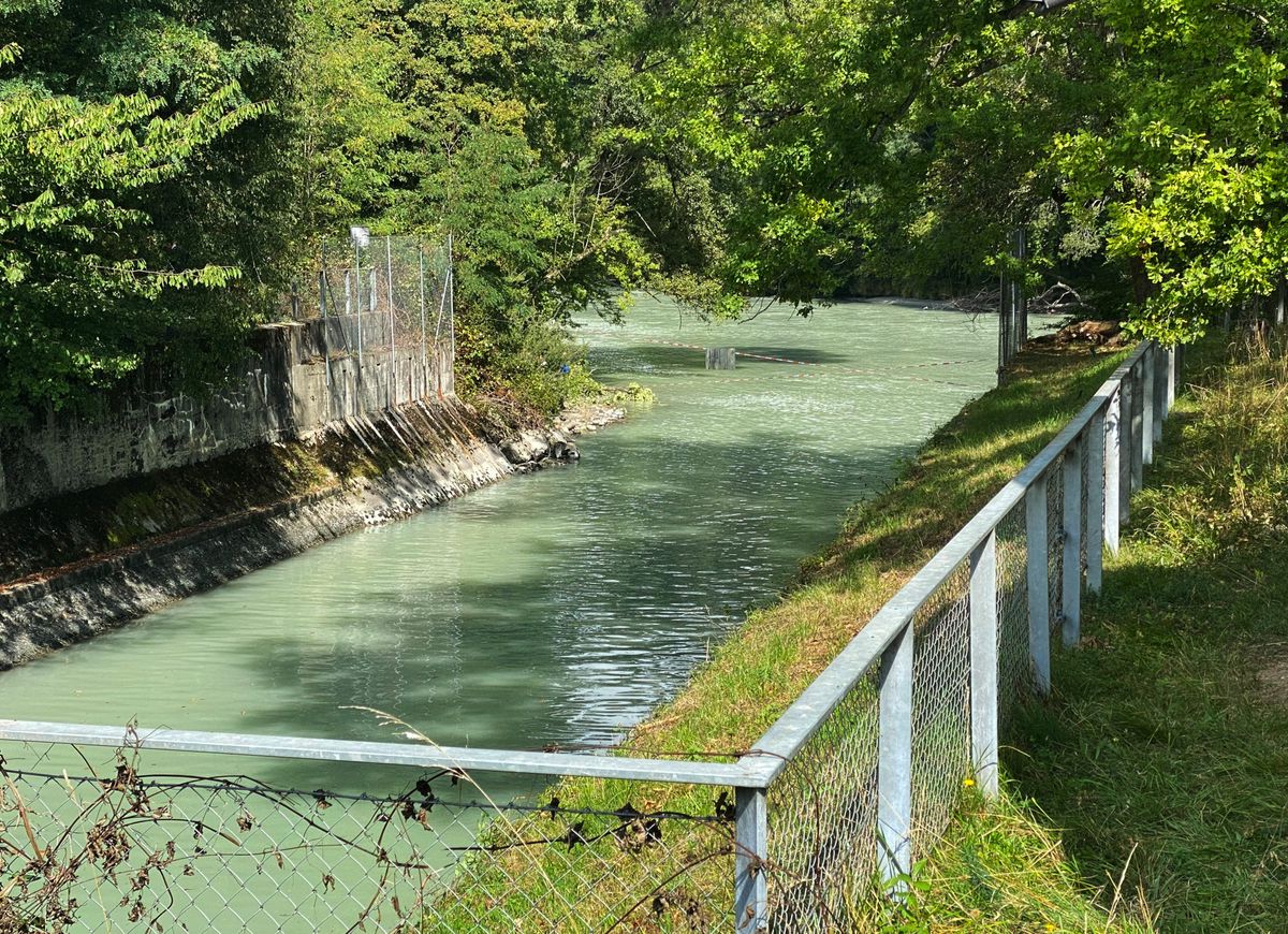 Vue de la rivière l'Arve à Genève avec une barrière en métal longeant un chemin sur la rive.