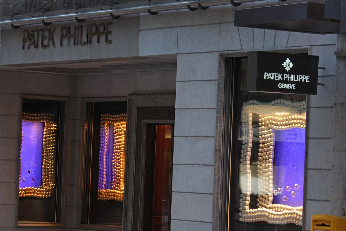 Vitrine de la boutique Patek Philippe à Genève sur la Rue du Rhône, éclairée par des lumières et avec un panneau indiquant ’GENEVE’.