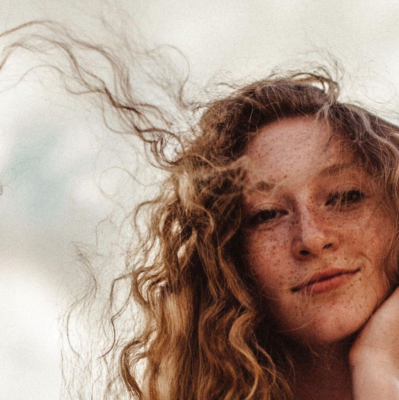 Femme aux cheveux bouclés regardant la caméra, avec les cheveux balayés par le vent.