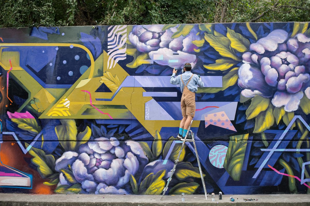Strassenkünstler sprüht Graffiti auf eine bunte Wand mit floralen Mustern in der Stadt.
