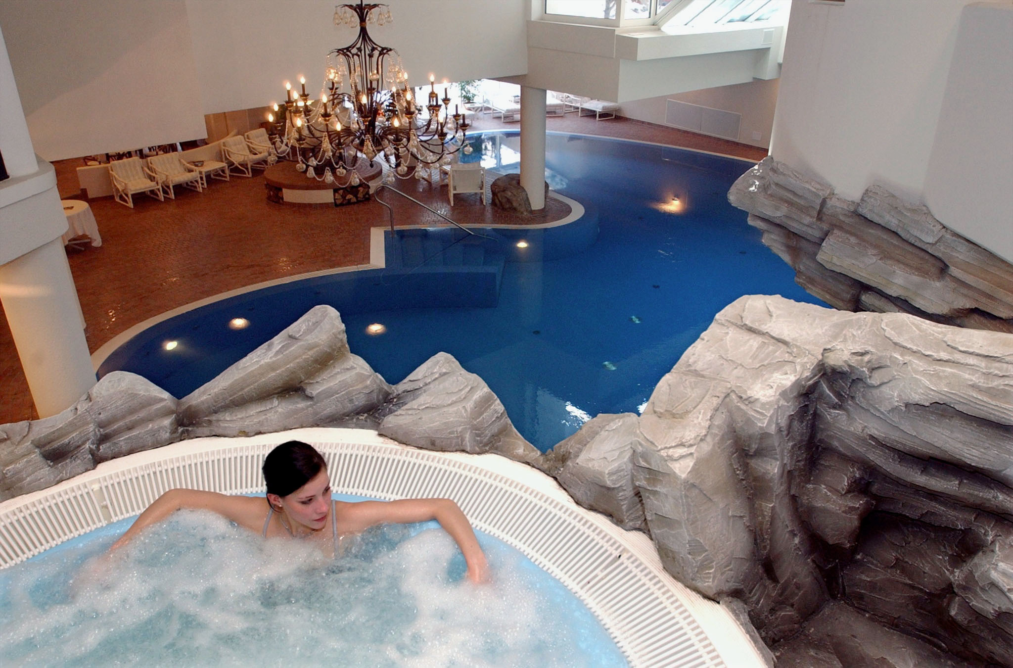 Un invité d’hôtel se détend dans un bain à remous de l’hôtel Walliserhof à Saas-Fee, avec la piscine de l’hôtel en arrière-plan.