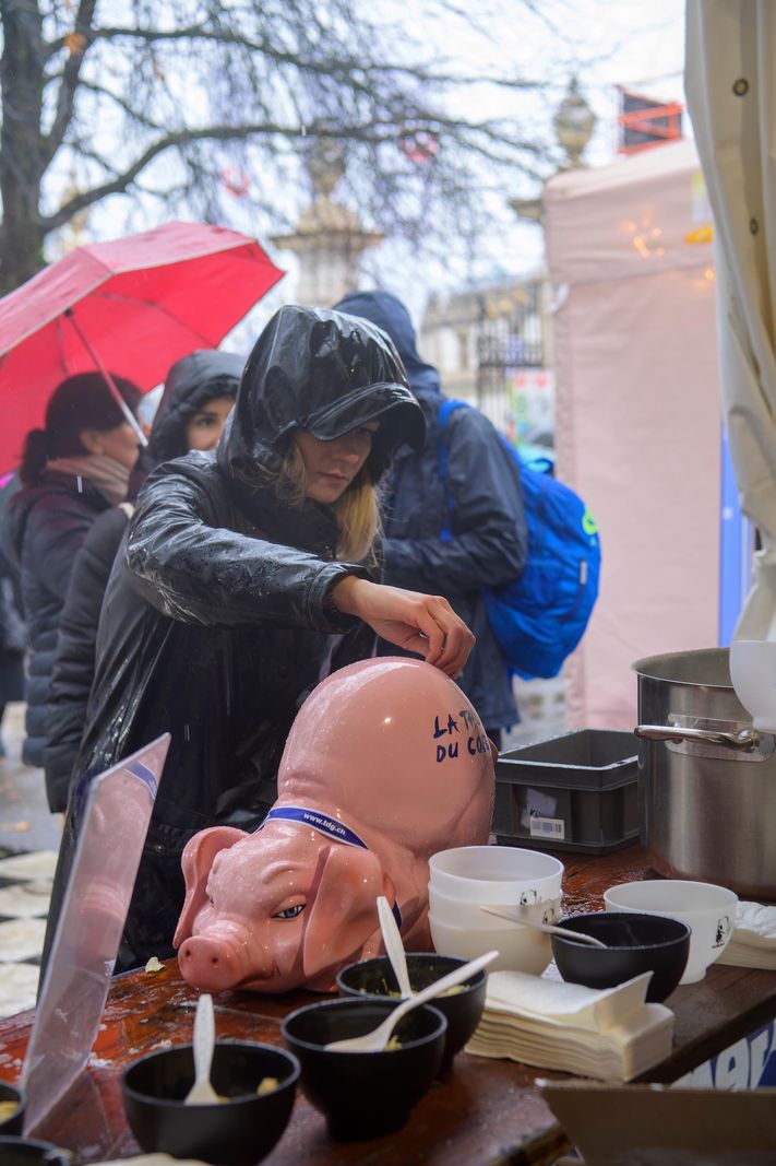 Participant de la 46e course de l’Escalade en tenue de pluie, devant un stand avec une tirelire cochon rose.