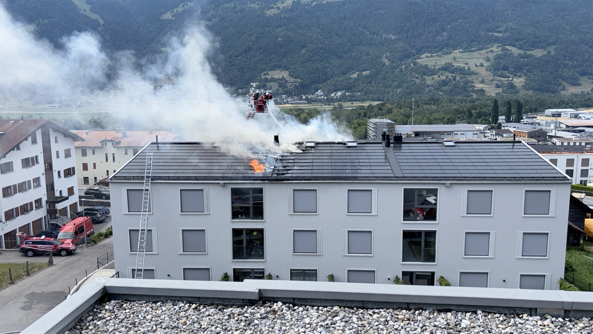 Brand auf dem Dach eines Mehrfamilienhauses: Flammen und Rauch steigen auf, Feuerwehr bekämpft das Feuer mit einer Leiter. Brand auf dem Dach eines Mehrfamilienhauses: Flammen und Rauch steigen auf, Feuerwehr bekämpft das Feuer mit einer Leiter.