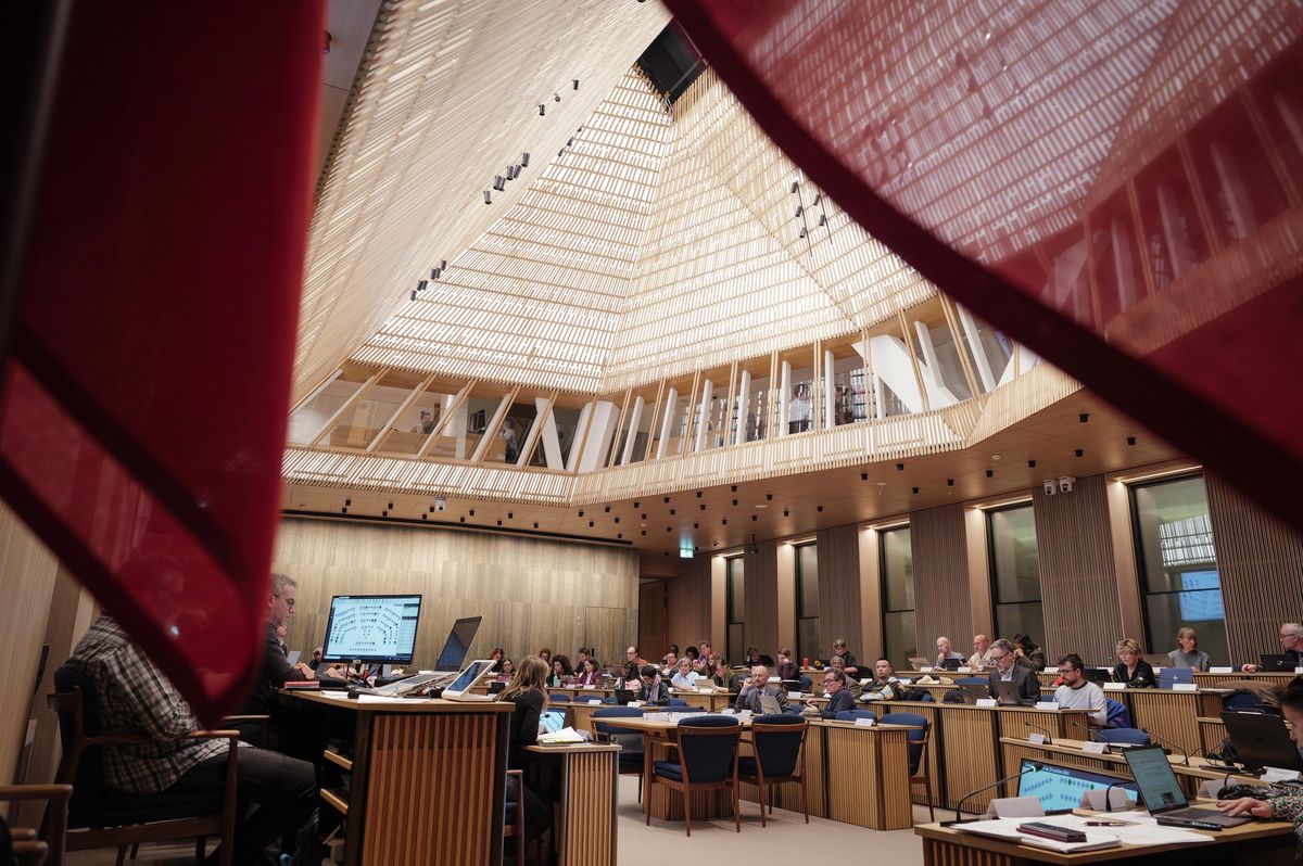 Réunion du Conseil municipal à l'Hôtel de Ville de Genève, avec des délégués assis autour d'une table sous un plafond architectural distinctif.