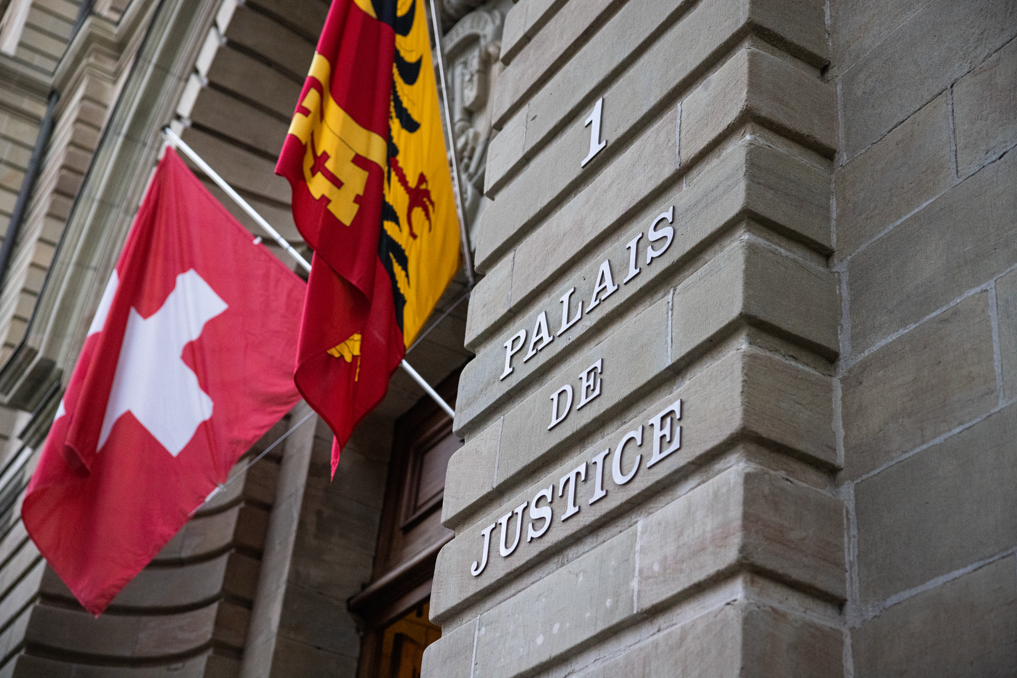 Entrée du Palais de Justice de Genève avec drapeaux suisse et genevois.