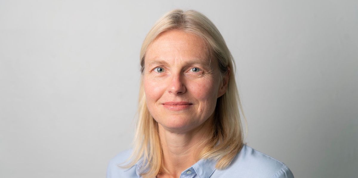 Portrait d'une femme blonde en chemise bleue avec un fond neutre.