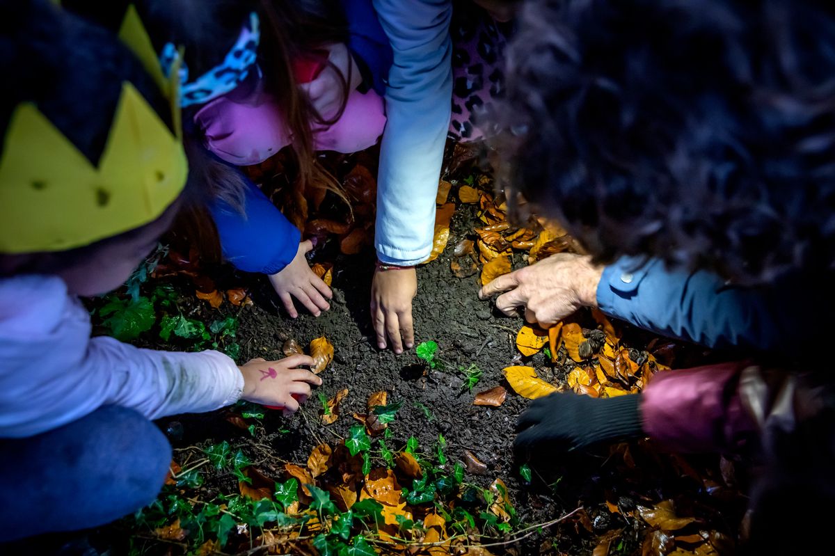 Des enfants et un adulte plantant ensemble dans la terre, entourés de feuilles d'automne à Genève en décembre 2022.