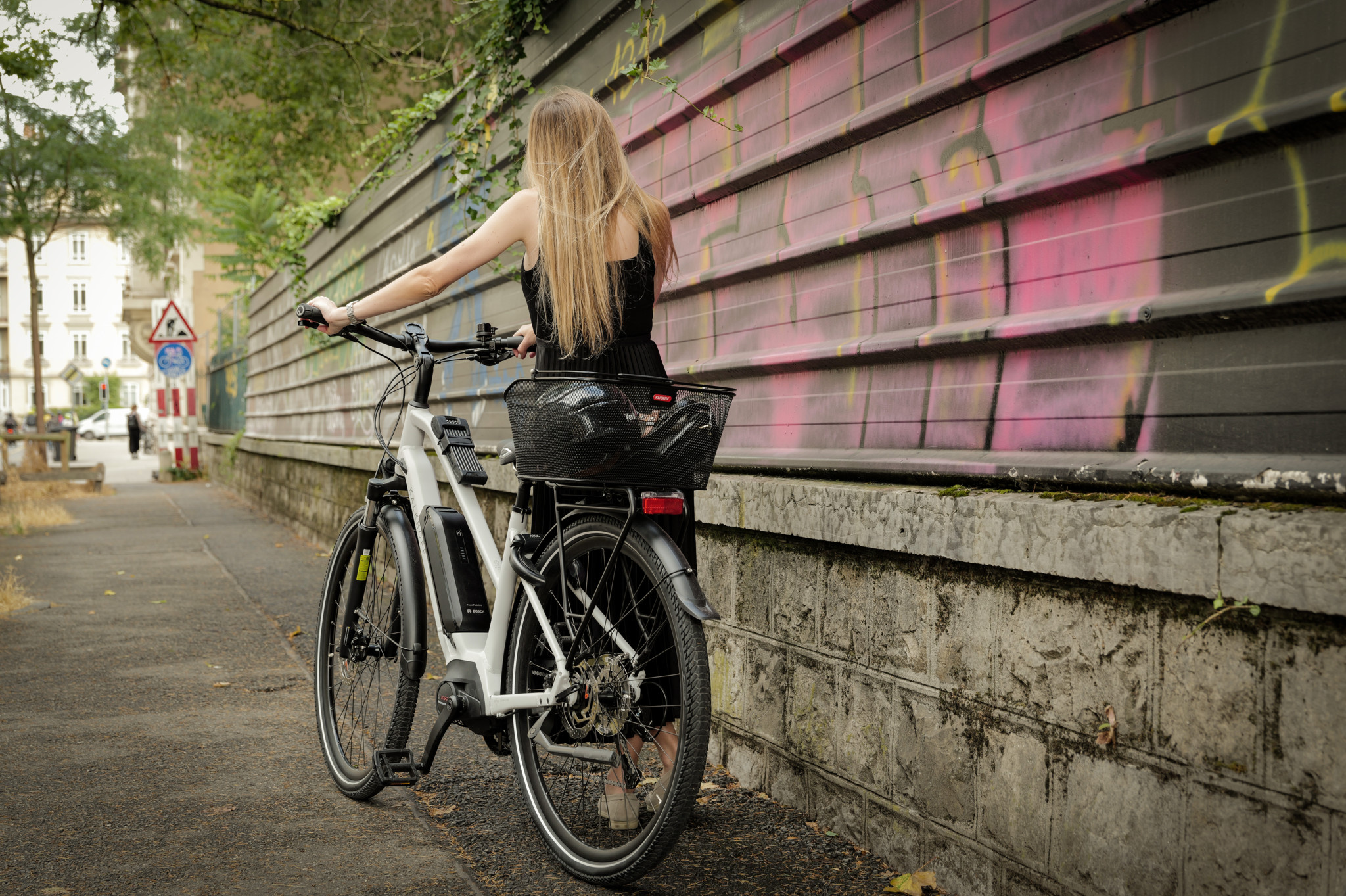 Une femme avec un nouveau vélo blanc, contre un mur couvert de graffitis à Genève.
