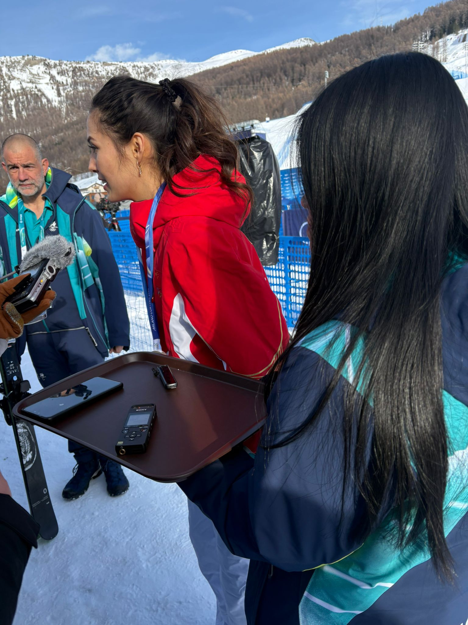 Un homme et deux femmes en vêtements d'hiver se tiennent sur une piste de ski lors d'un entretien.
