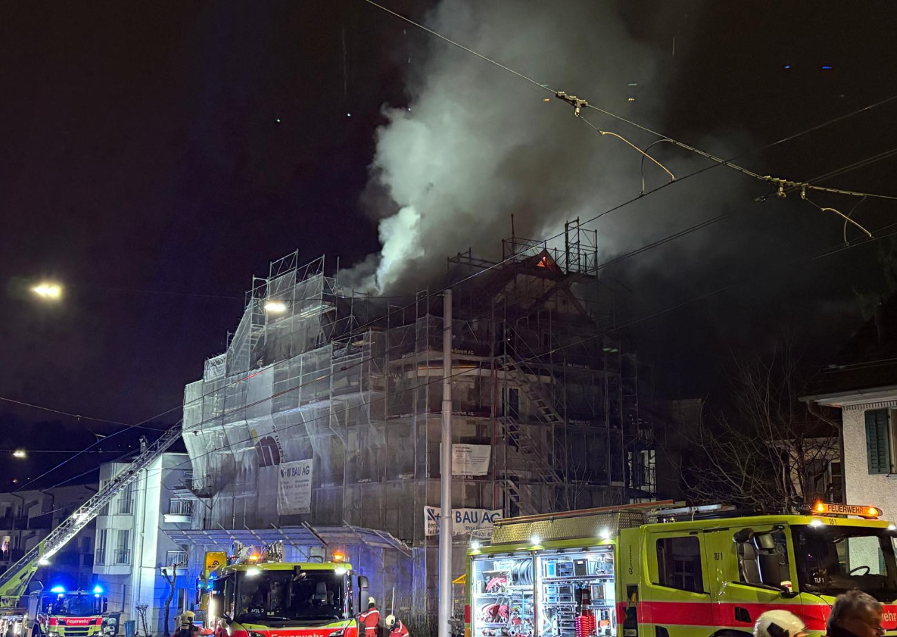 Nachtaufnahme eines Gebäudebrandes in einem Gerüst, mit Feuerwehrfahrzeugen und Rauchentwicklung.