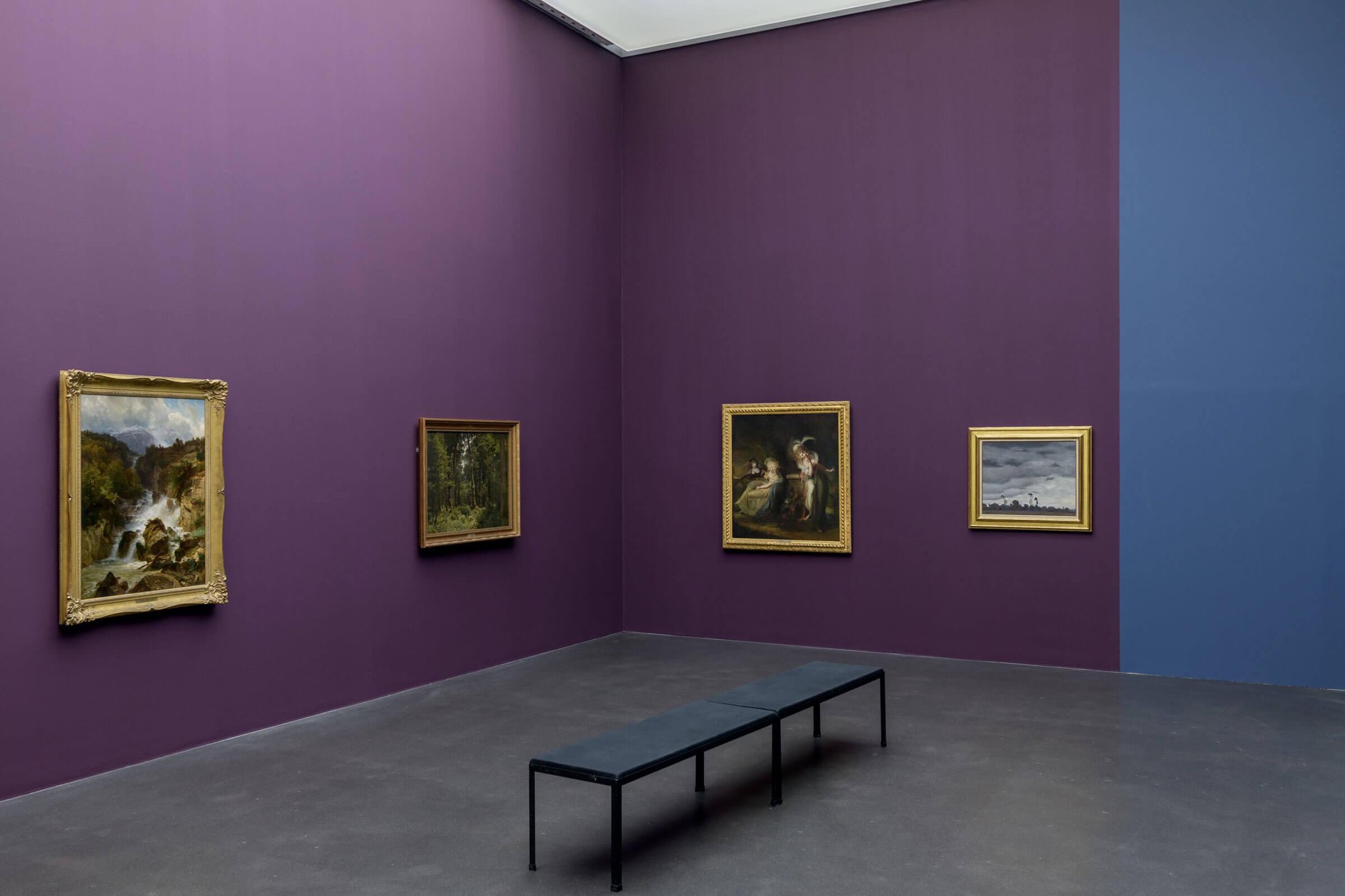 Salle d’exposition d’art avec murs violets, contenant cinq tableaux encadrés de différentes tailles et un banc noir au centre.