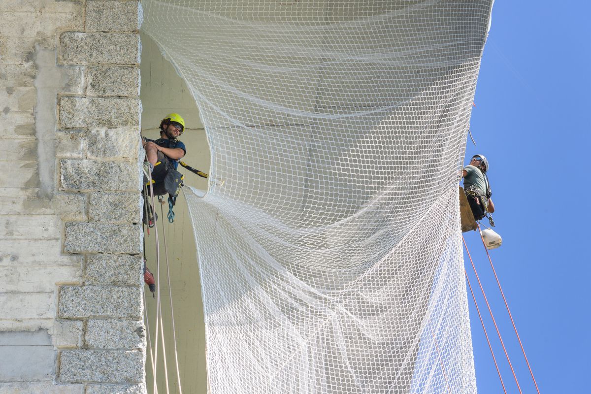 Workers tied with ropes install safety nets under the Buting Bridge.