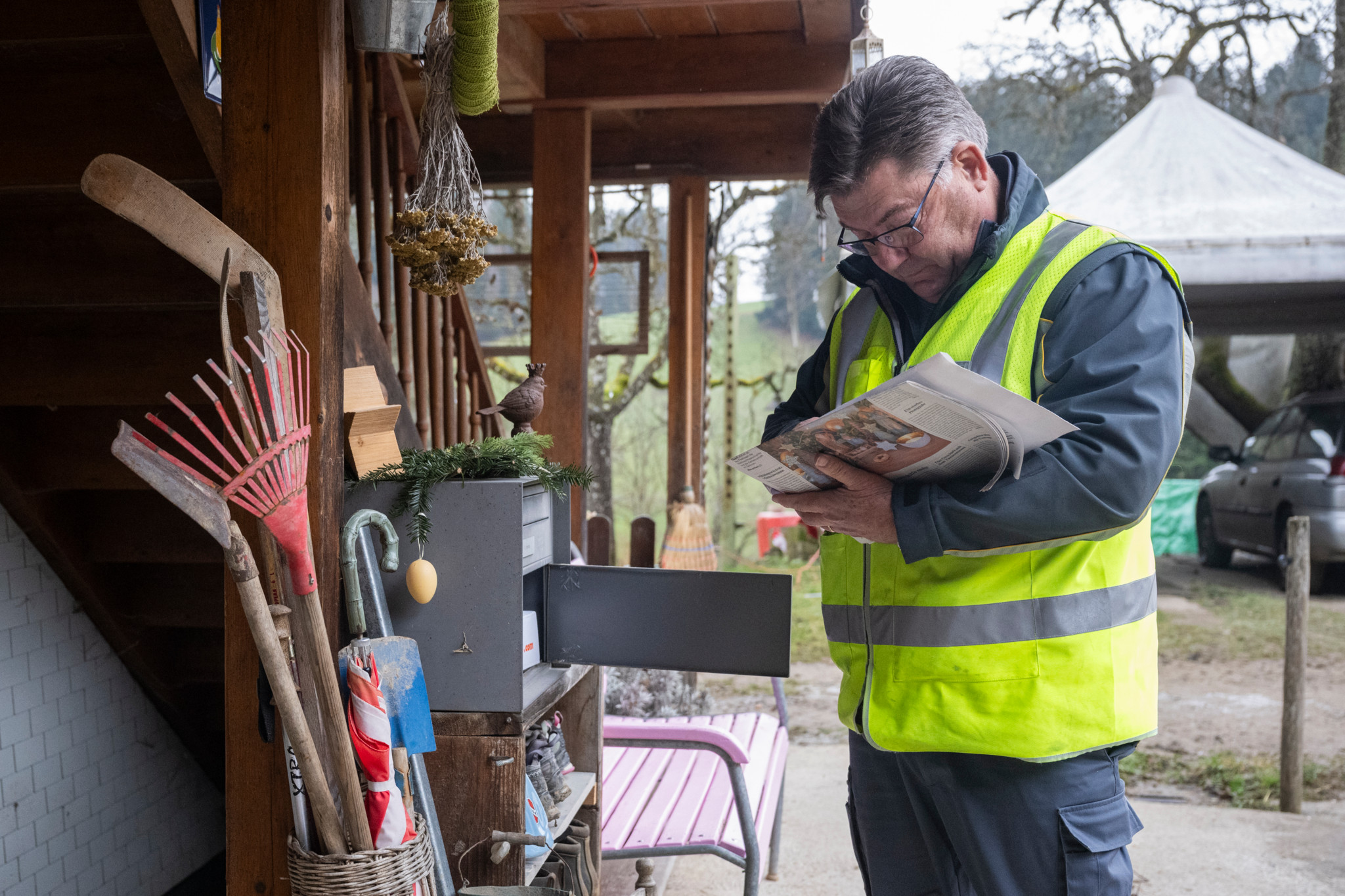 Briefträger Erich Marti liest am 24. Dezember 2025 in Hinterfultigen neben einem Briefkasten eine Zeitung.