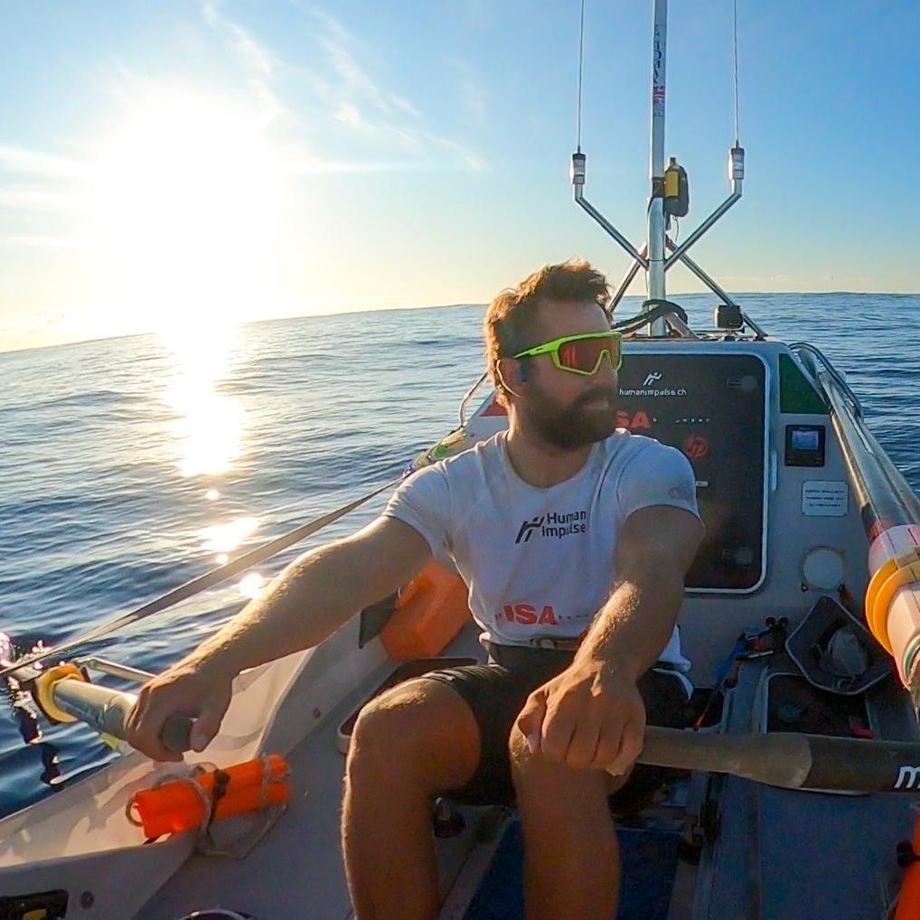 Un homme ramant seul sur un canoë au lever du soleil sur une mer calme.