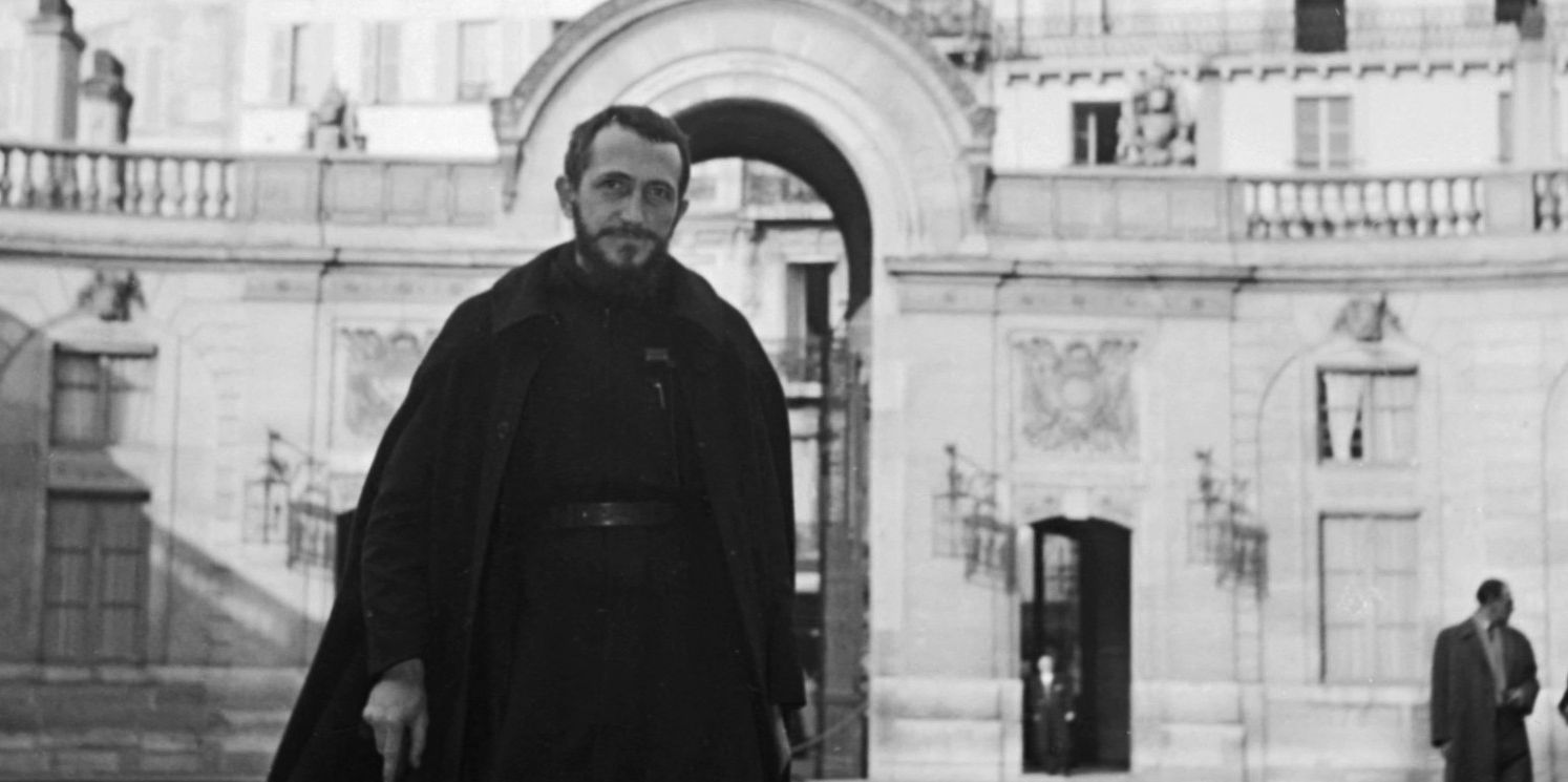 L'Abbé Pierre en 1954, marchant vers l'Élysée pour sensibiliser au problème des sans-logis. Grande architecture parisienne en arrière-plan.