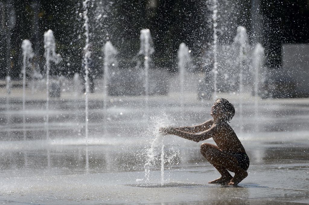 Un enfant s'amuse avec les jets de la fontaine de la place des Nations, ce dimanche 30 aout 2015 a Geneve. Le thermometre affiche jusqu'a 33 degres. (KEYSTONE/Martial Trezzini)