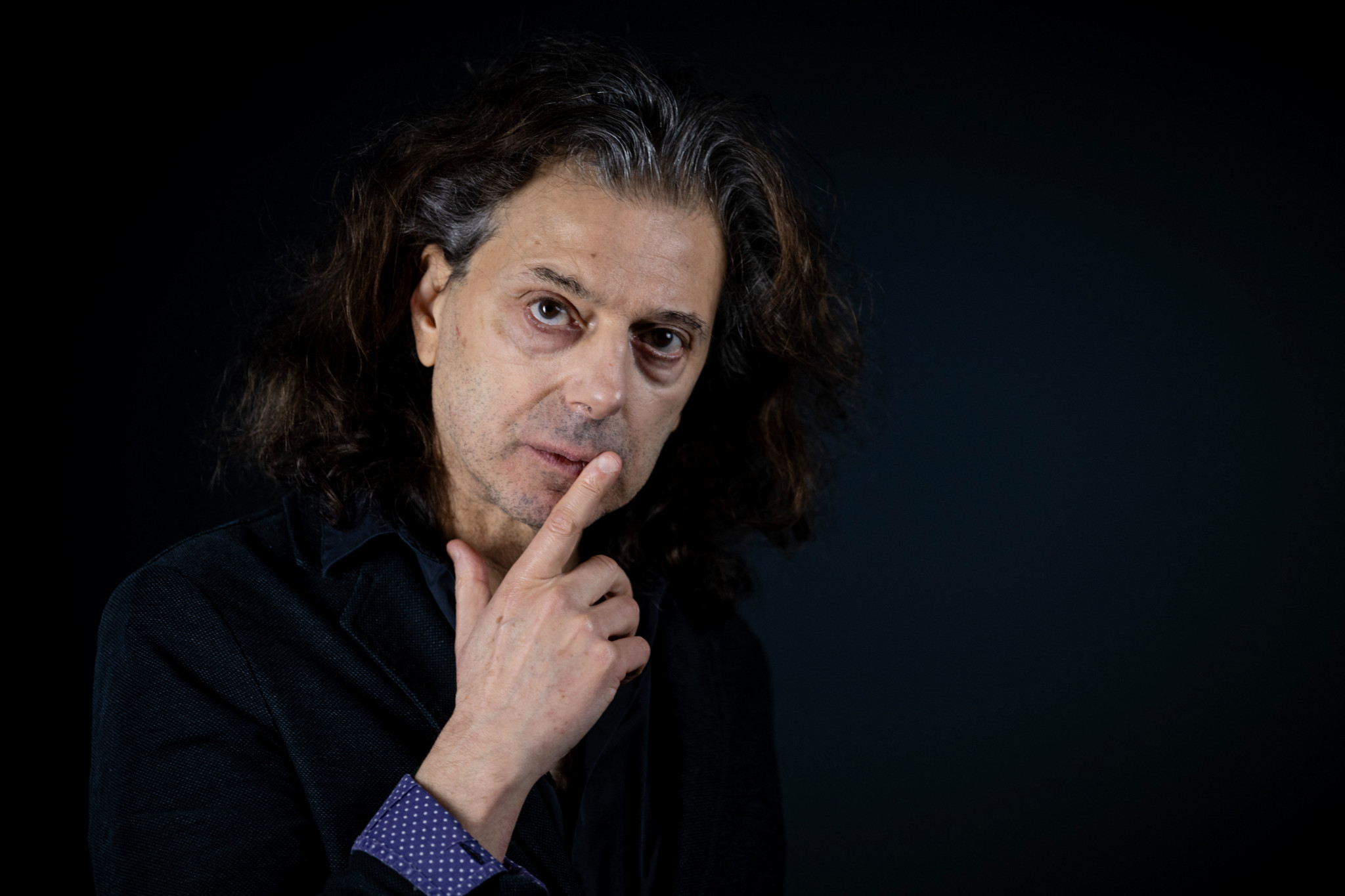 L’écrivain et philosophe français Éric Sadin, cheveux longs, pose pensif le doigt sur la joue lors d’une séance photo à Paris.