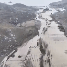 Vue aérienne d’une vallée inondée entourée de collines, avec des plantations partiellement submergées.