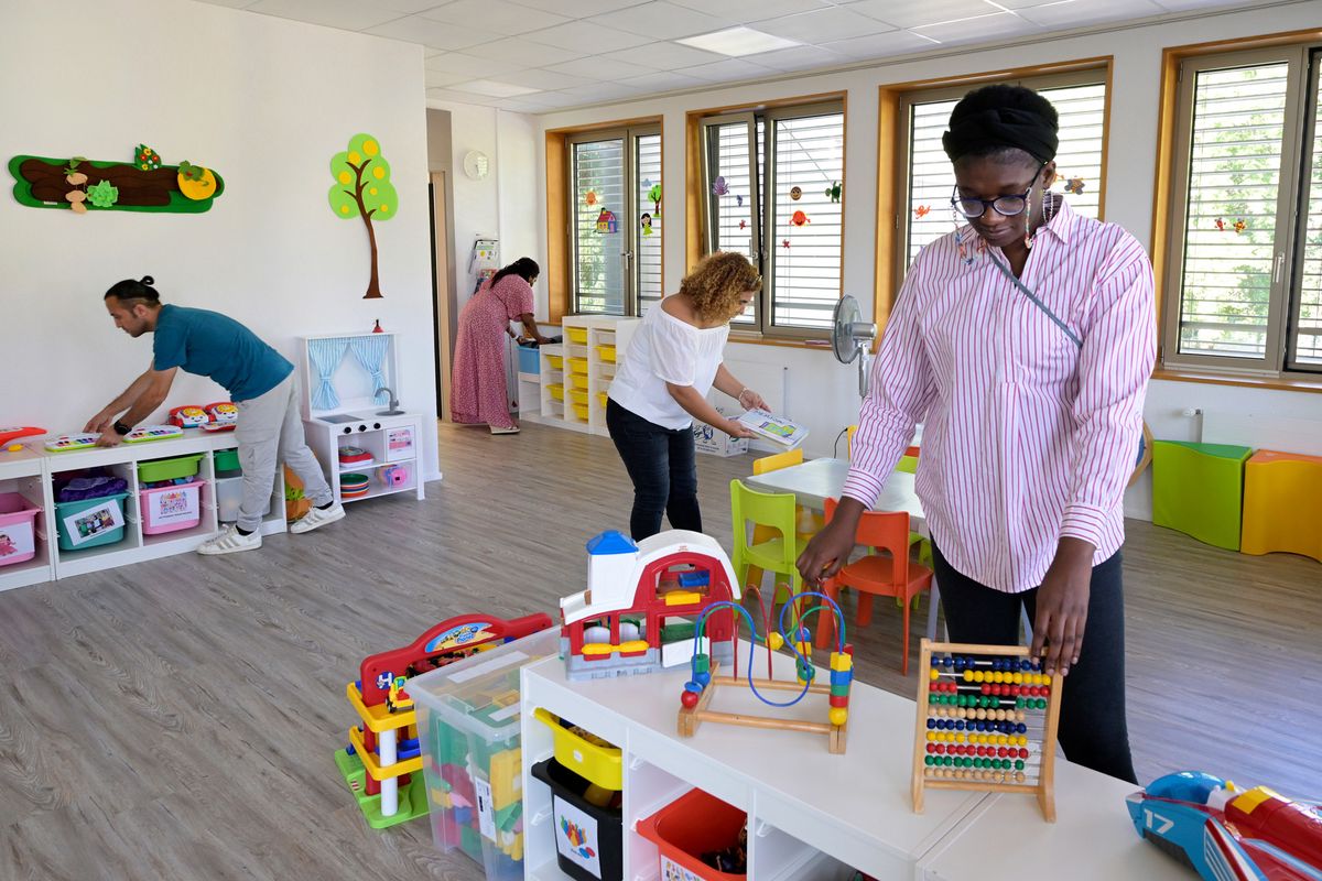 Présentation du nouveau centre de formation EVAM à Aigle le 22 août 2024, avec une halte-garderie installée dans les locaux. Quatre adultes organisent divers jouets dans une salle lumineuse.