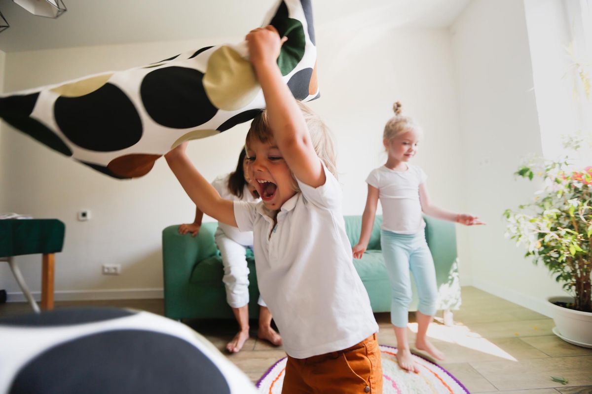 Enfants jouant dans un salon lumineux avec un coussin, une ambiance intérieure authentique.