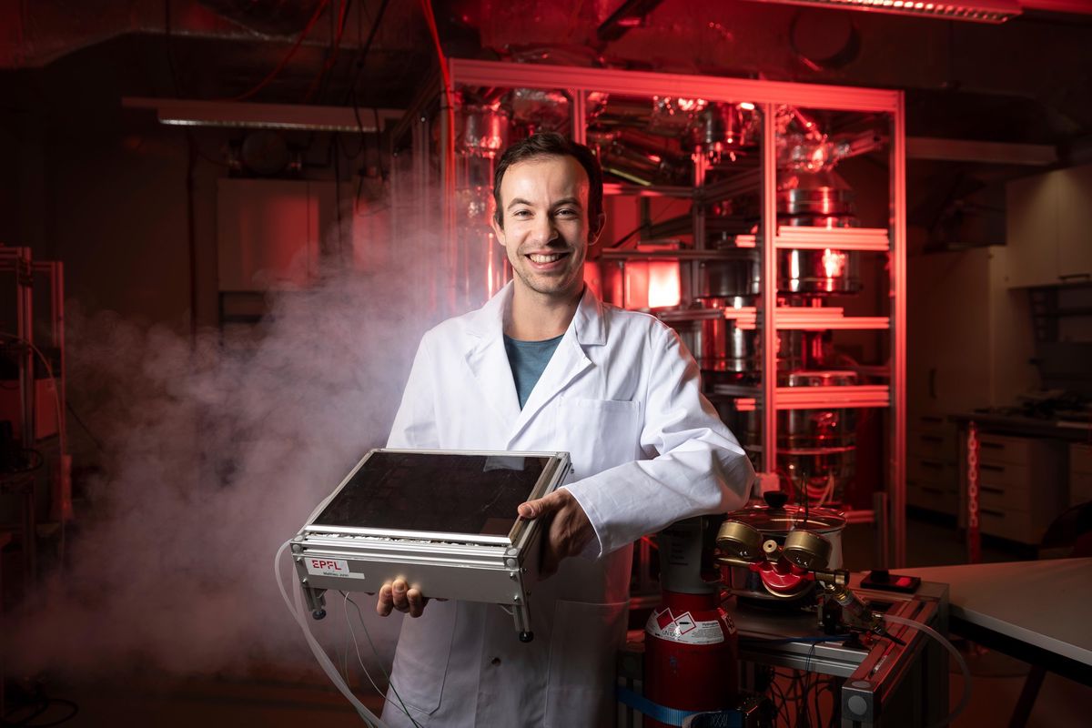 Chercheur de l’EPFL tenant un réchaud à hydrogène solaire dans un laboratoire d’Écublens. Fond rouge et environnement scientifique.